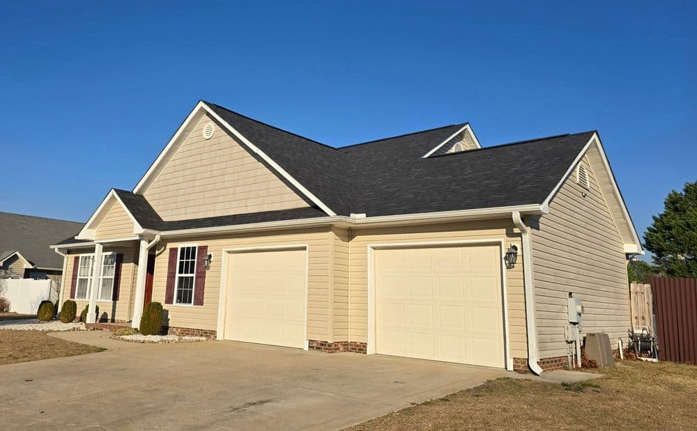 Modern beige house with two garages and manicured lawn under clear blue sky.
