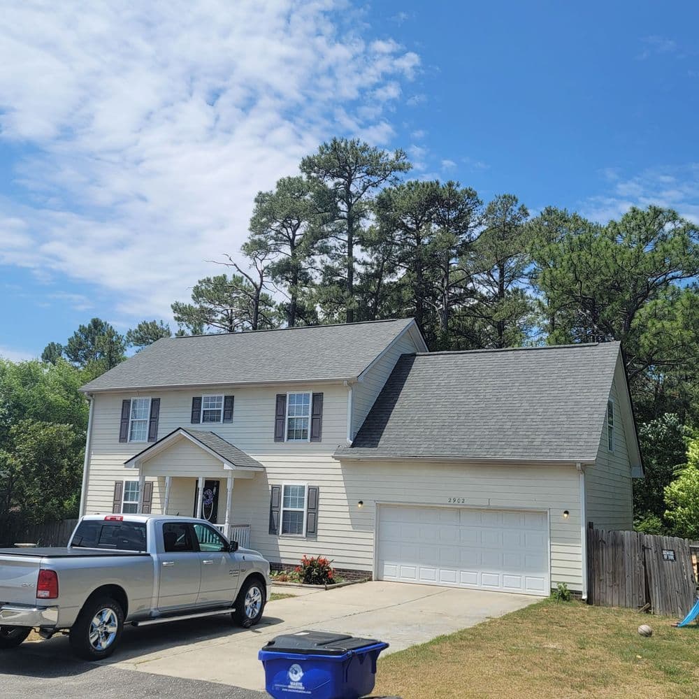Two-story suburban house with a garage, surrounded by trees and clear blue sky.