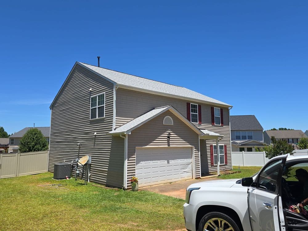 Side view of a two-story house with a gray exterior and garage, under a clear blue sky.