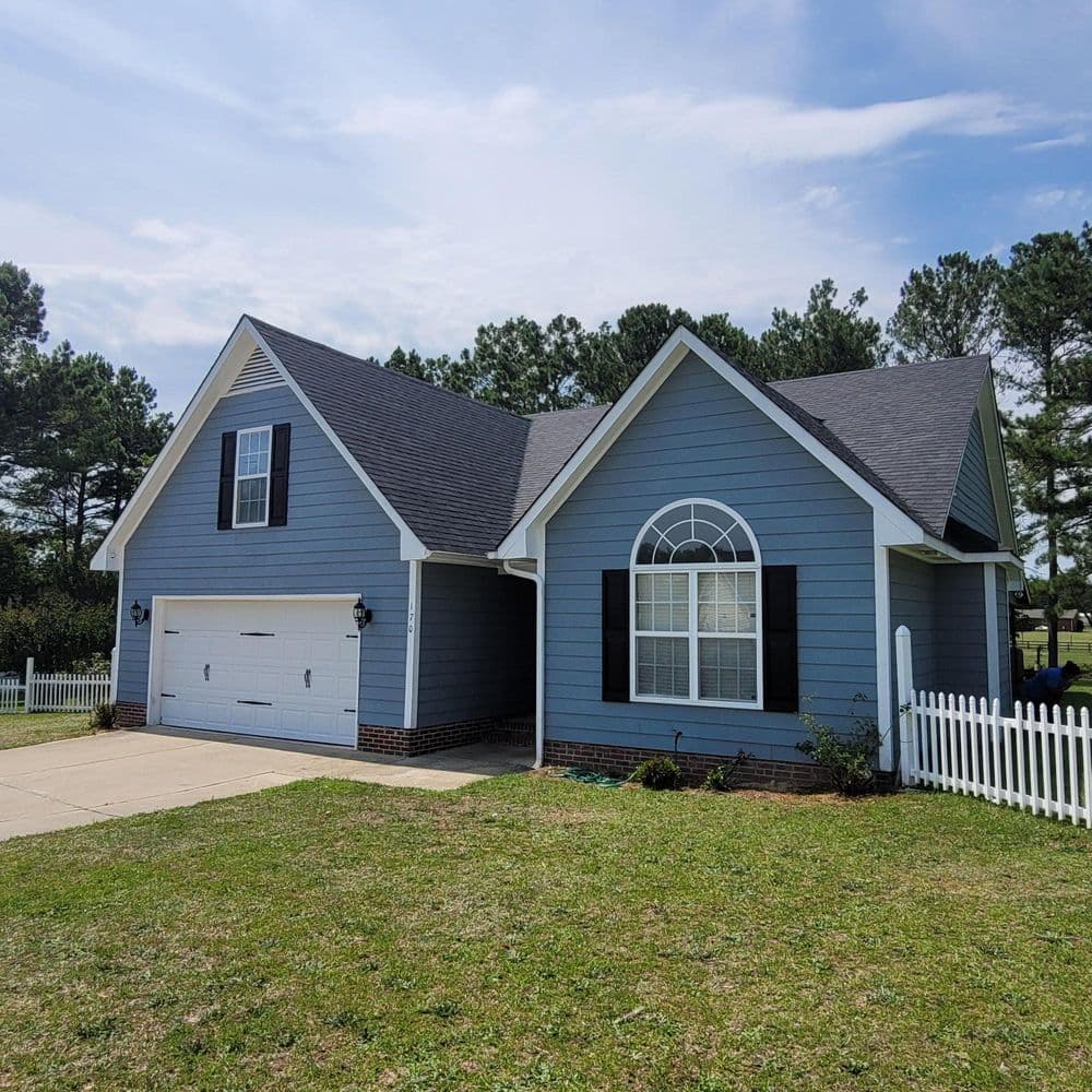 Blue suburban house with a front lawn, white picket fence, and garage on a sunny day.