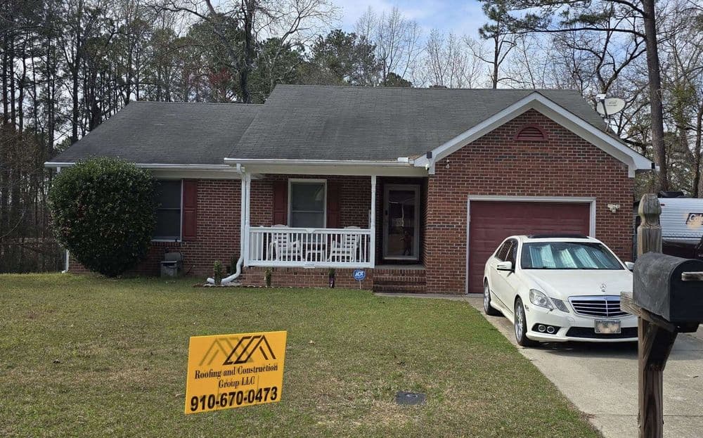 Brick house with porch, green lawn, and parked car, featuring a construction sign in front.