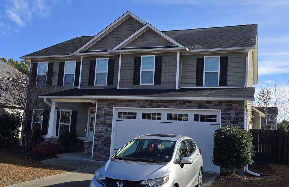 Two-story suburban home with stone accents, white garage, and parked gray car in driveway.