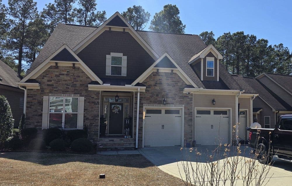 Modern stone house with a spacious front yard and double garage under clear blue sky.