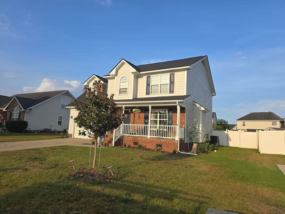 Two-story brick and siding home with front porch, landscaped yard, and clear blue sky.