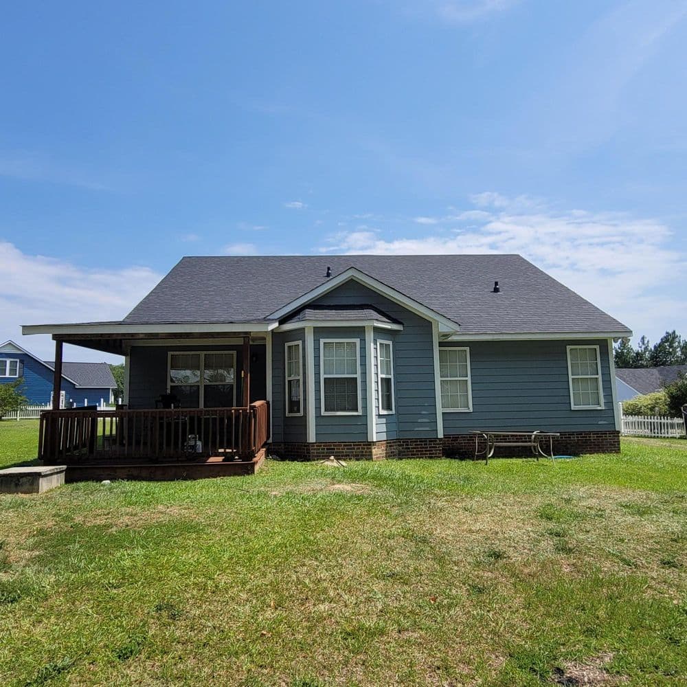 Blue suburban house with a front porch on a sunny day, surrounded by a green lawn.