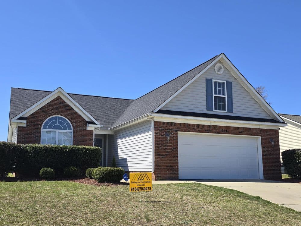 Single-family home with brick facade, gray siding, garage, and "For Sale" sign in yard.