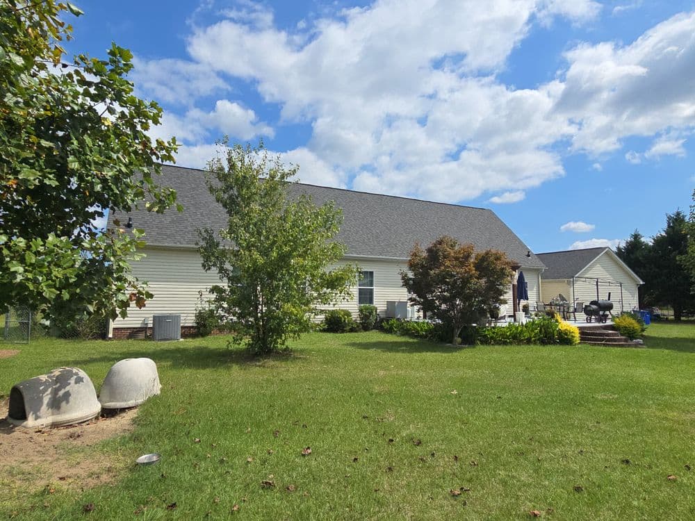 White house with a gray roof, surrounded by greenery and a sunny blue sky.