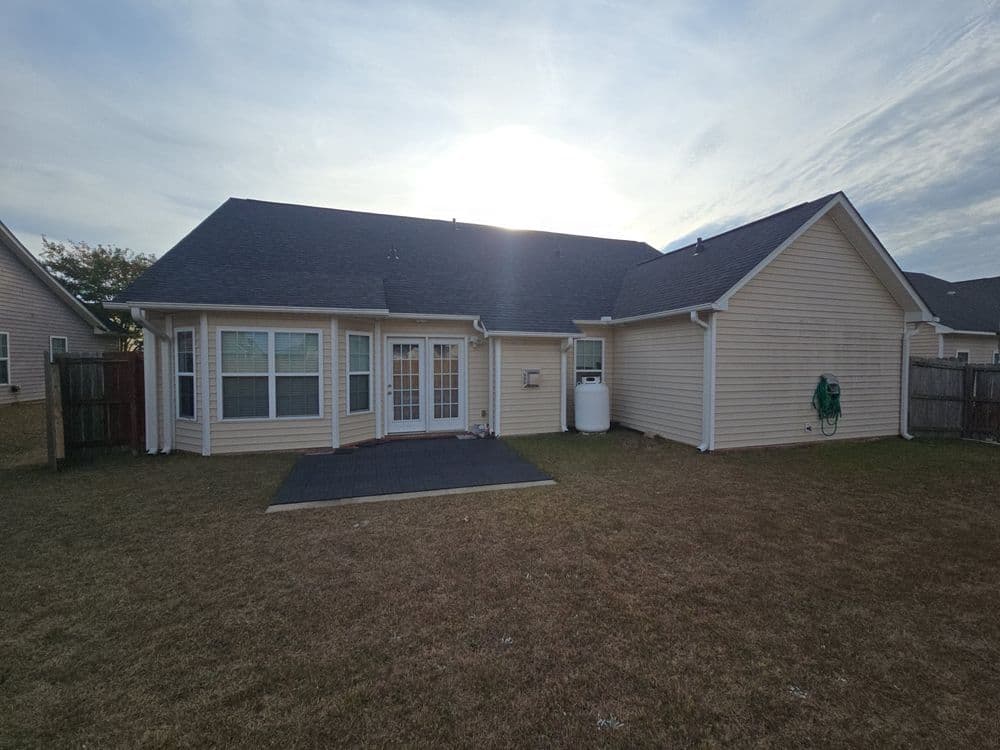 Backyard view of a home with patio, grass lawn, and sunset sky in the background.