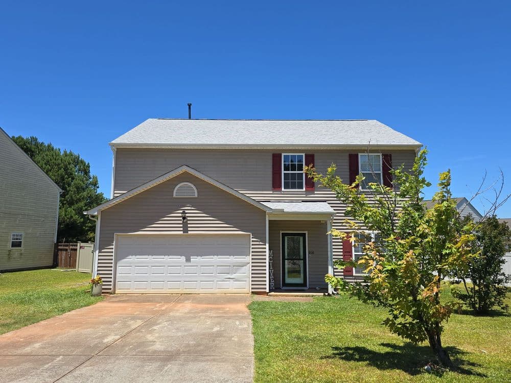 Two-story house with a garage, red shutters, and landscaped front yard under a clear blue sky.