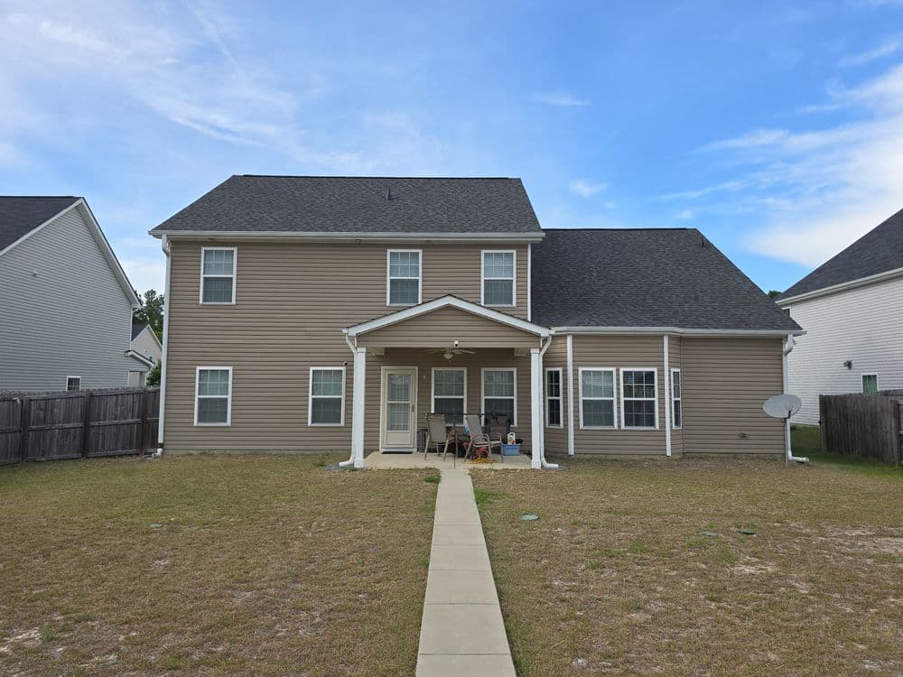 Two-story beige house with porch and backyard, featuring a brick pathway and neighboring homes.