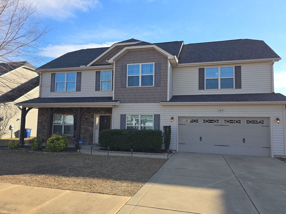 Two-story modern home with stone accents, manicured lawn, and double garage on a clear day.