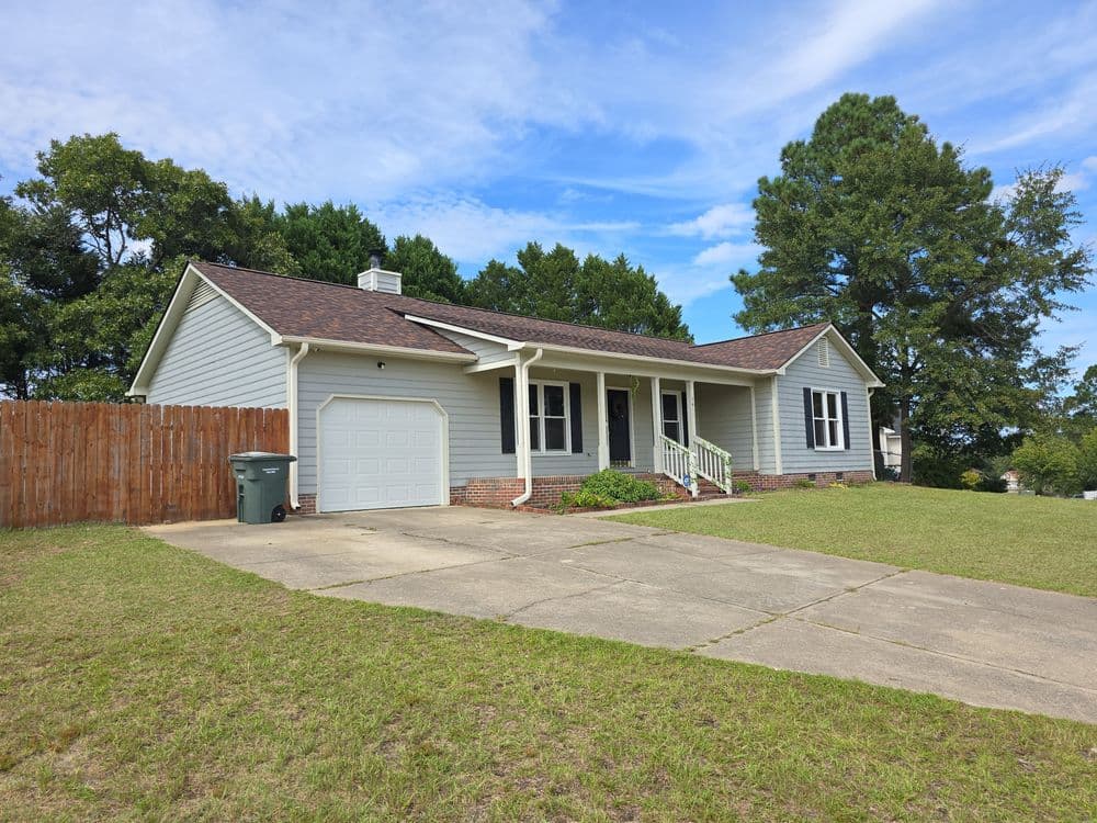 Single-story gray house with garage, green lawn, and trees under a blue sky.