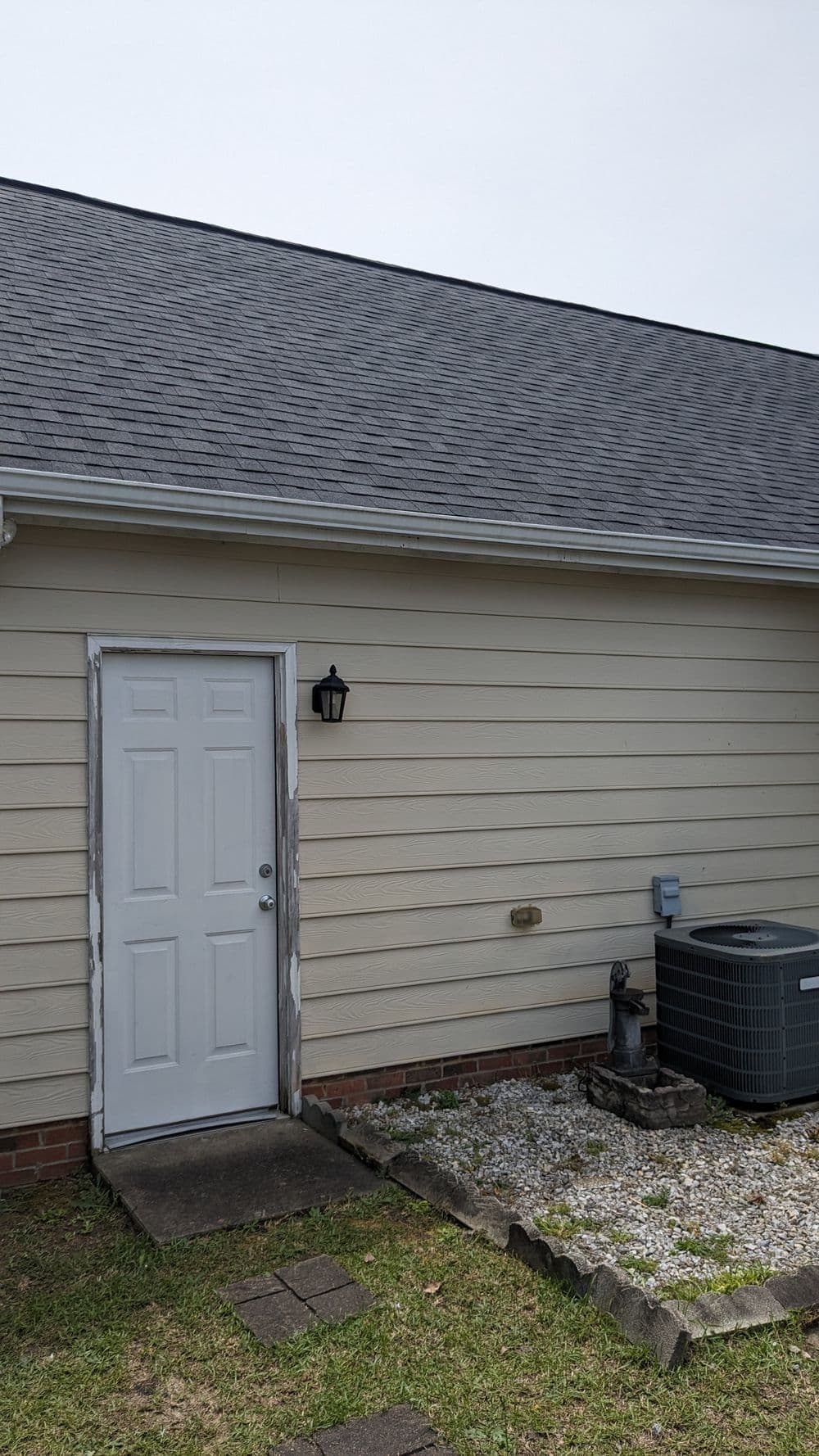 Side view of a beige house with a white door, light fixture, and air conditioning unit.