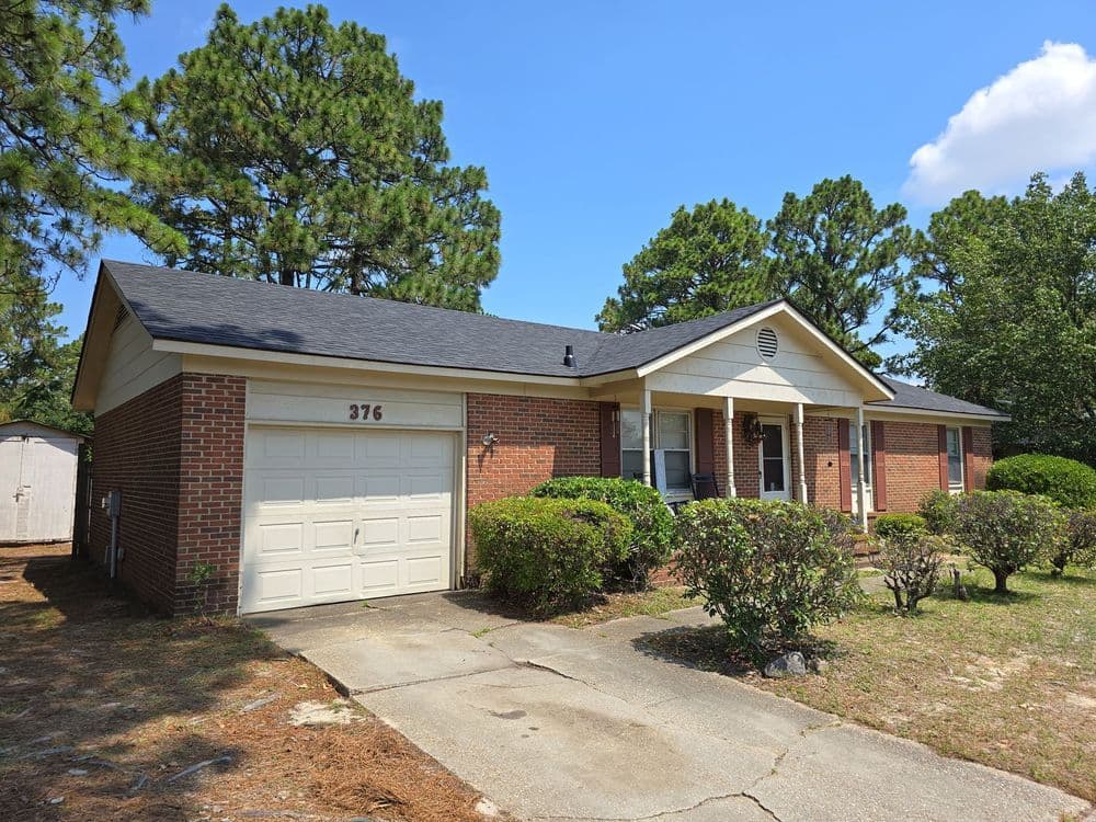 Single-story brick home with garage, front yard shrubbery, and blue sky in the background.
