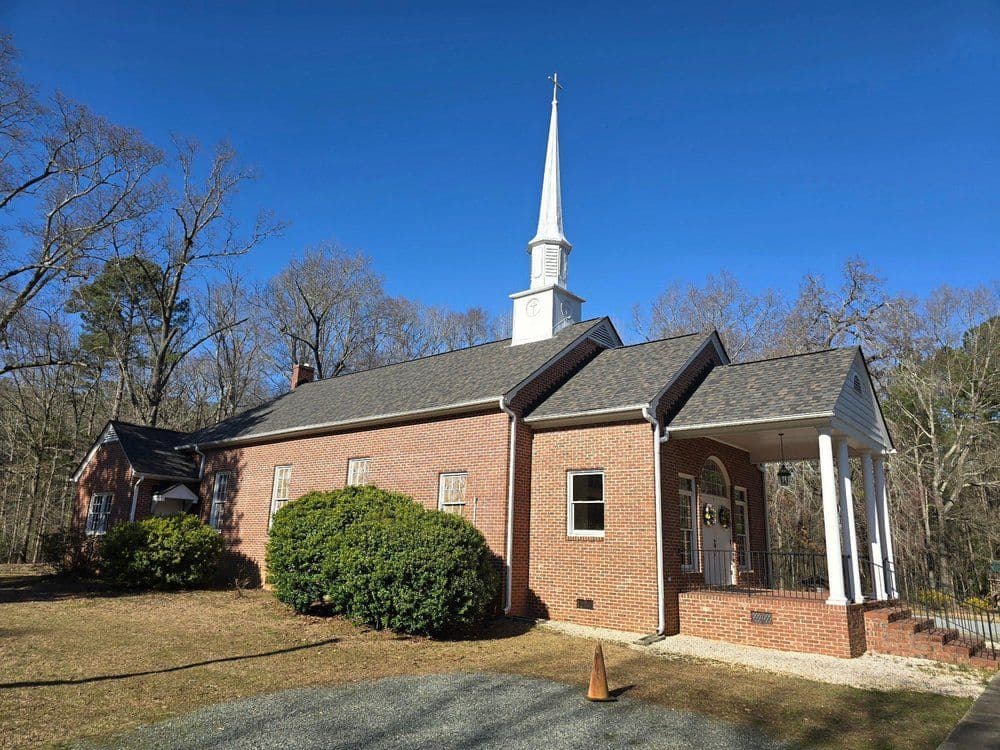 Historic brick church with steeple, surrounded by trees and a clear blue sky.