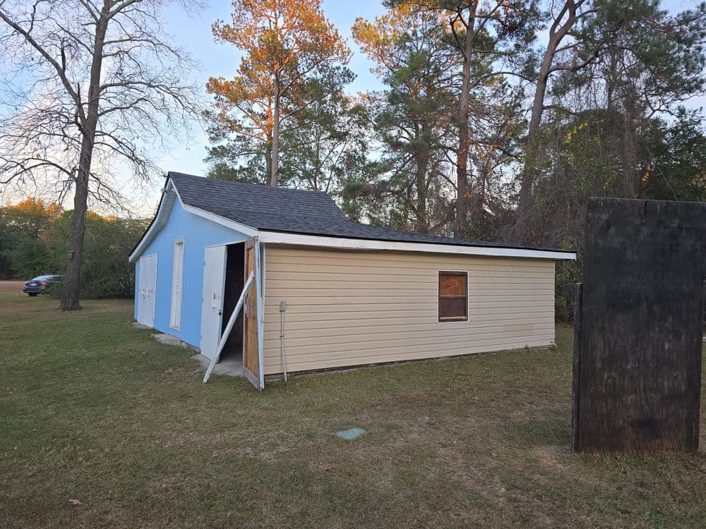 Small house with a blue and beige exterior, surrounded by trees and grassy area.