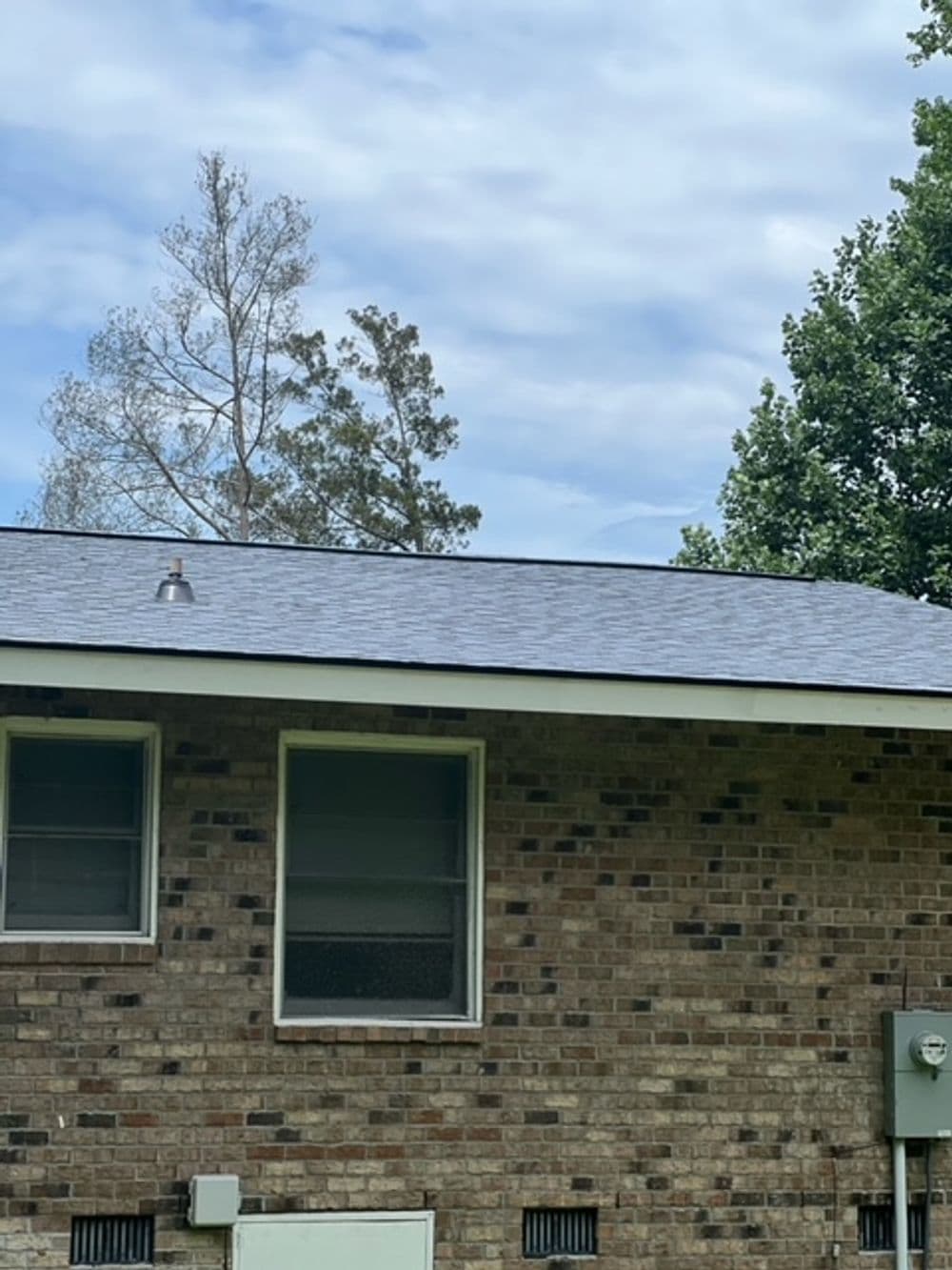 Newly installed gray shingle roof on a brick house under a cloudy sky.