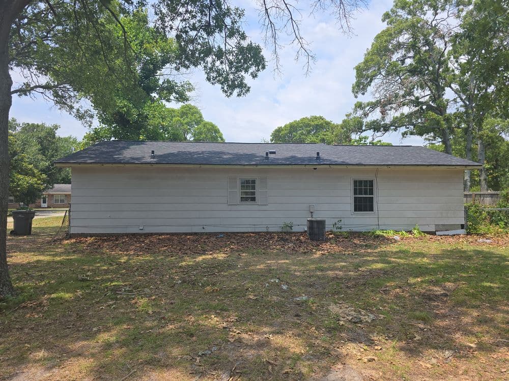 Side view of a single-story house with a new roof, surrounded by trees and grass.