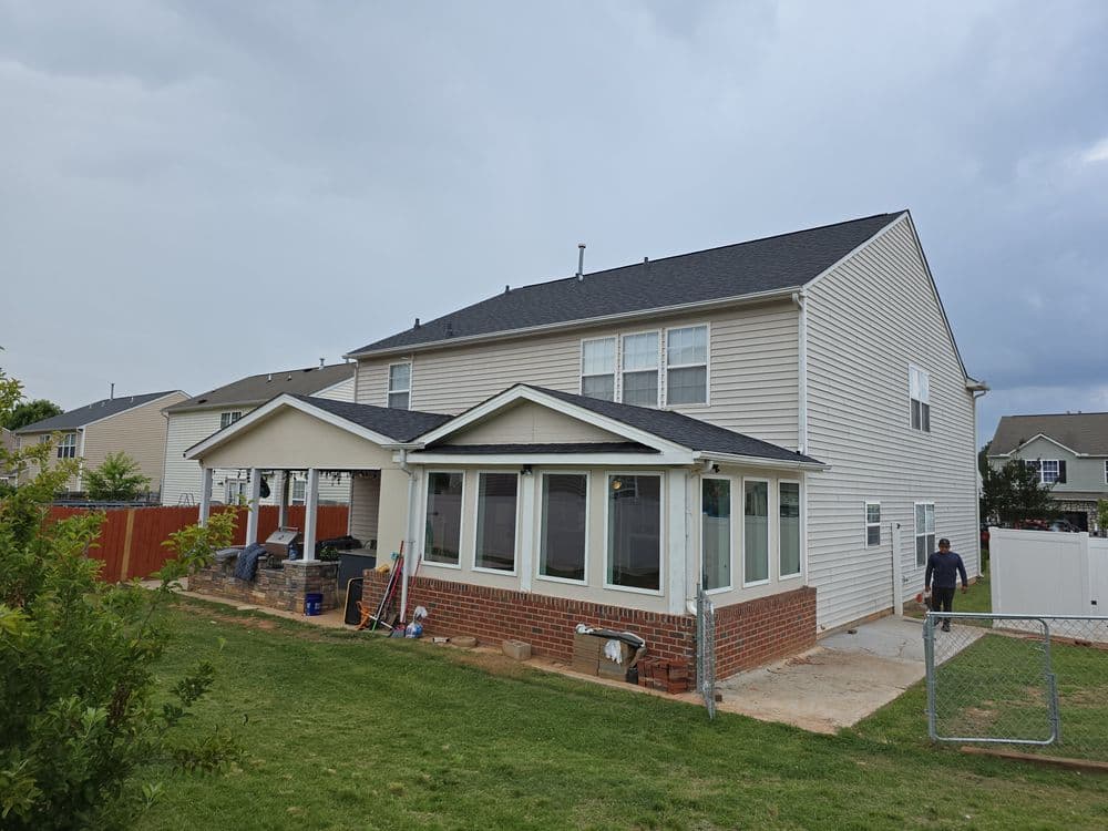 Rear view of a modern two-story home with a porch and landscaped yard under cloudy skies.