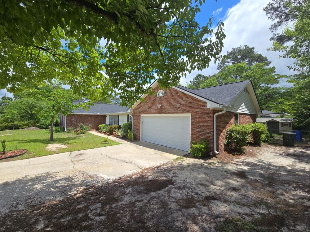 Brick home with a garage, surrounded by greenery and a clear blue sky on a sunny day.