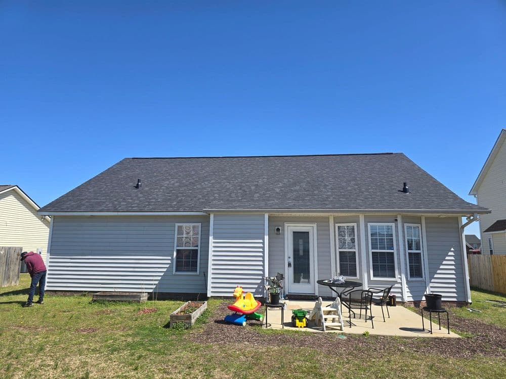 Single-story house with backyard, patio furniture, and children's toys on a sunny day.