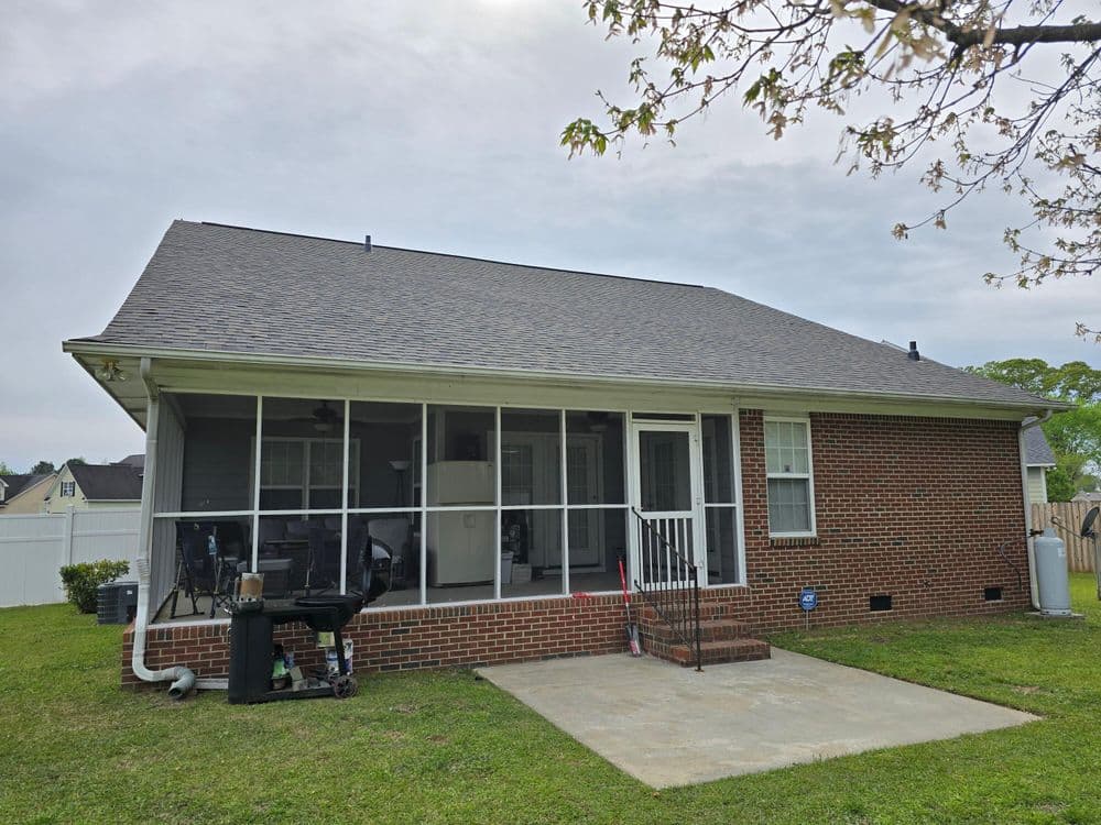 Brick house with screened porch and green lawn, showcasing a spacious backyard setting.