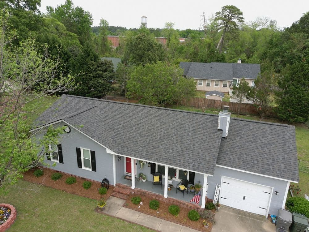 Aerial view of a charming gray house with a welcoming porch and landscaped yard.