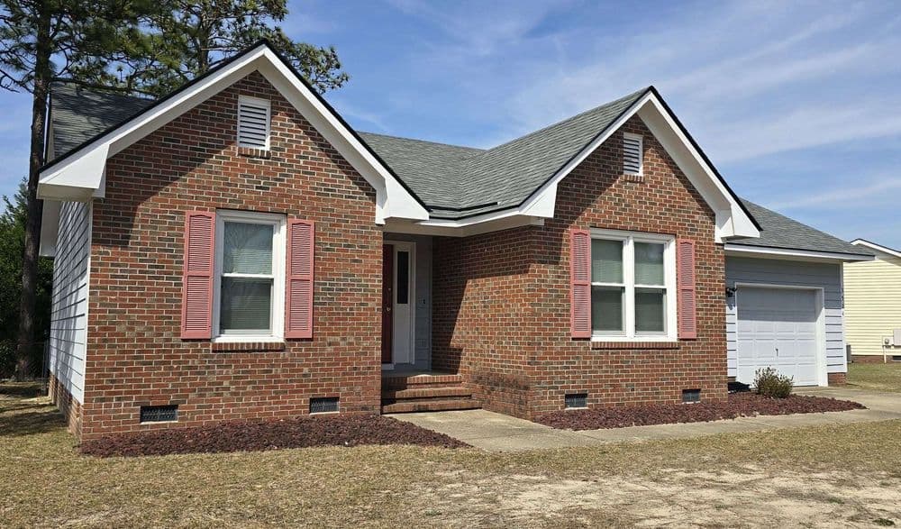 Brick bungalow with pink shutters, front porch, and garage in a residential neighborhood.