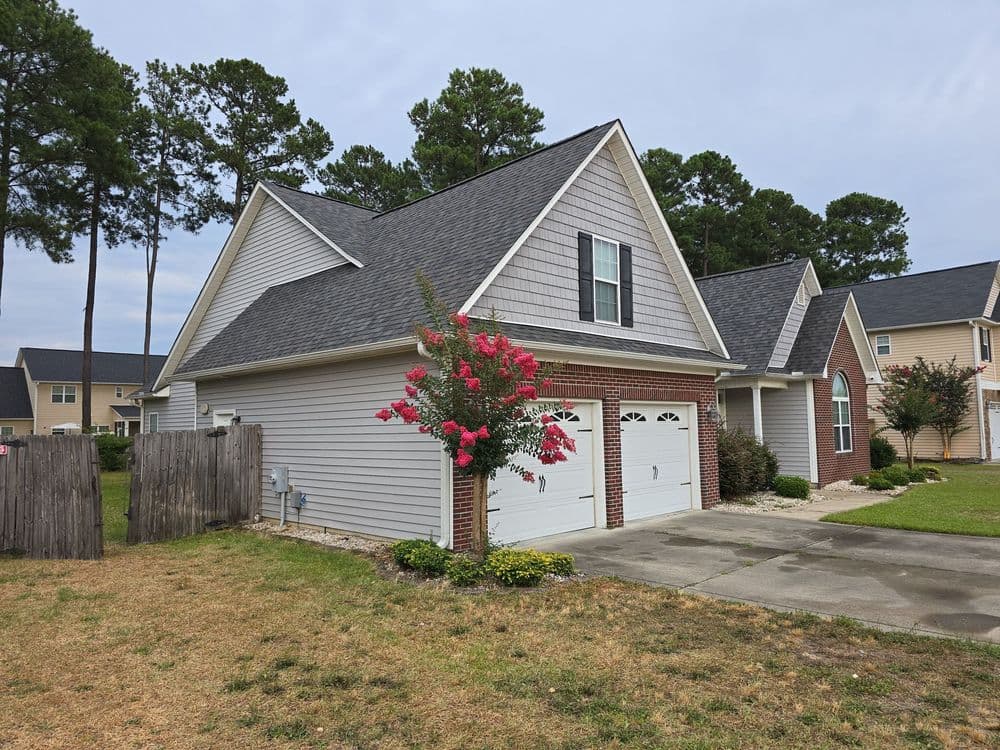 Modern two-story house with a garage, blooming pink flowers, and a green lawn in a serene neighborhood.