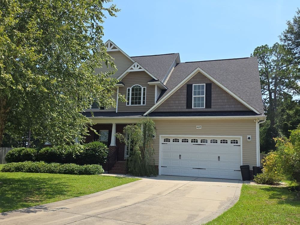 Two-story family home with a lush lawn, garage, and trees under a clear blue sky.