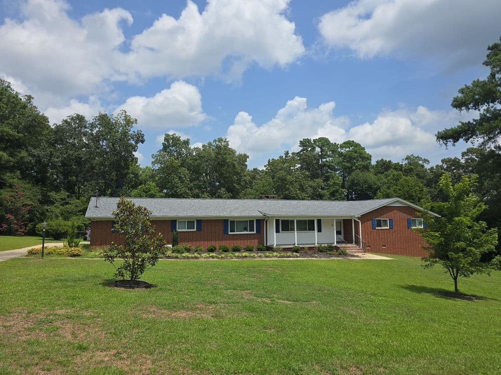 Modern brick ranch-style home surrounded by lush greenery and blue sky. Ideal family residence.