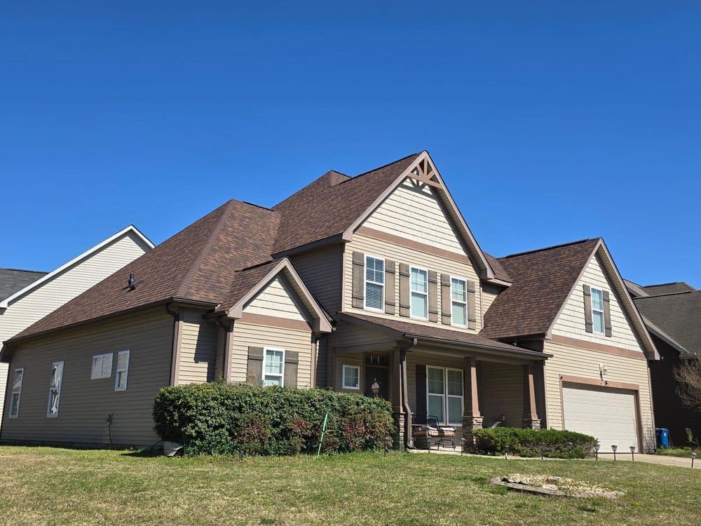 Two-story suburban home with brown siding, gabled roof, and front porch on a sunny day.