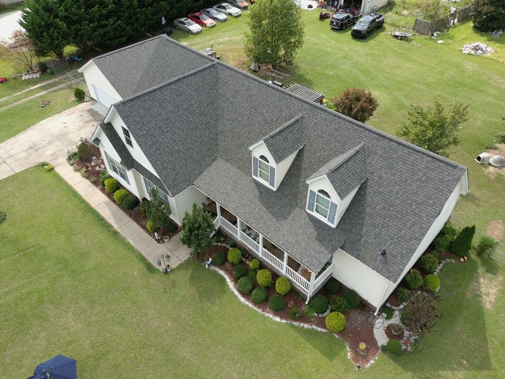 Aerial view of a modern home with landscaped yard and driveway, parked cars nearby.