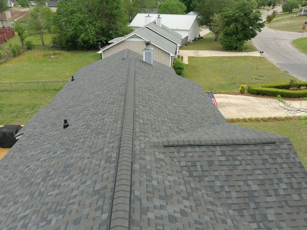 Aerial view of a gray shingled roof on suburban homes with a green lawn and street visible.