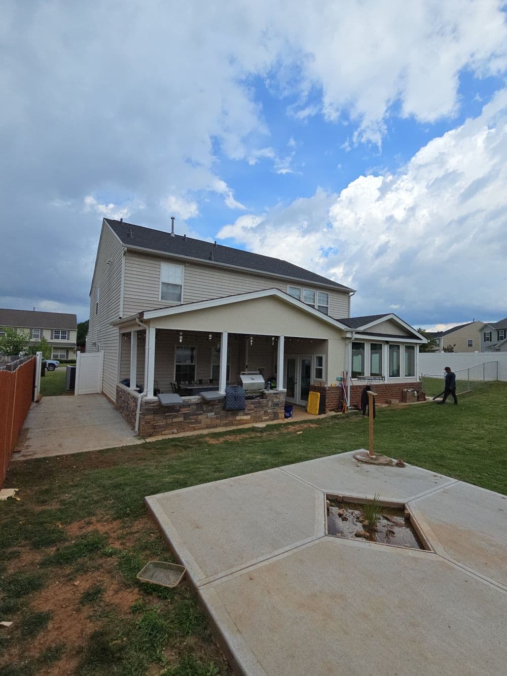 Two-story house with covered patio, backyard, and cloudy sky in suburban setting.