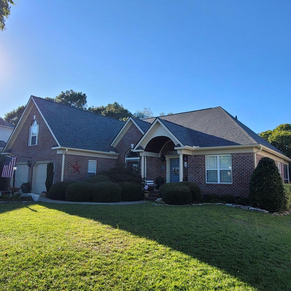 Modern brick house with a well-maintained lawn and landscaped shrubs under a clear blue sky.