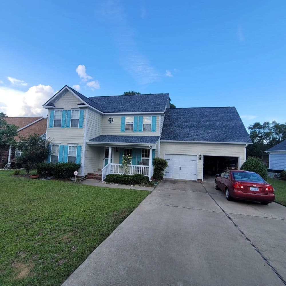 Two-story yellow house with a porch, green lawn, and red car in the driveway.