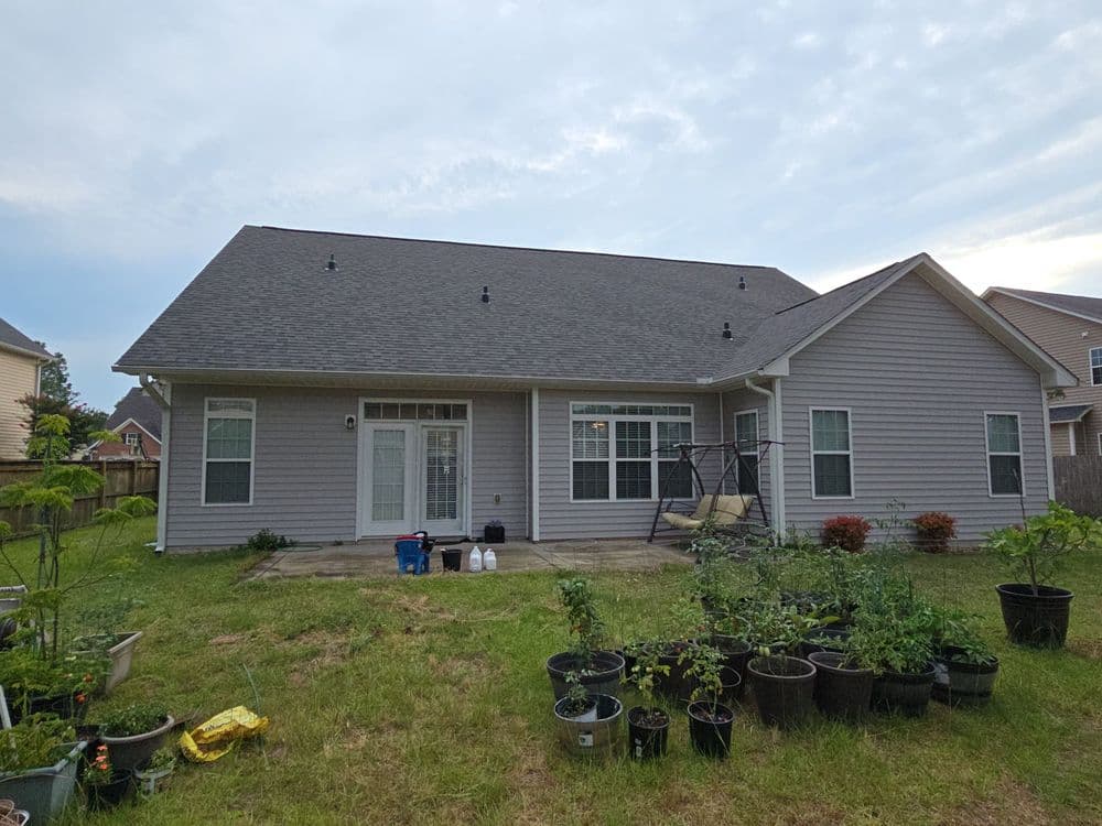 Backyard view of a home with a light gray exterior, patio, and garden planters.