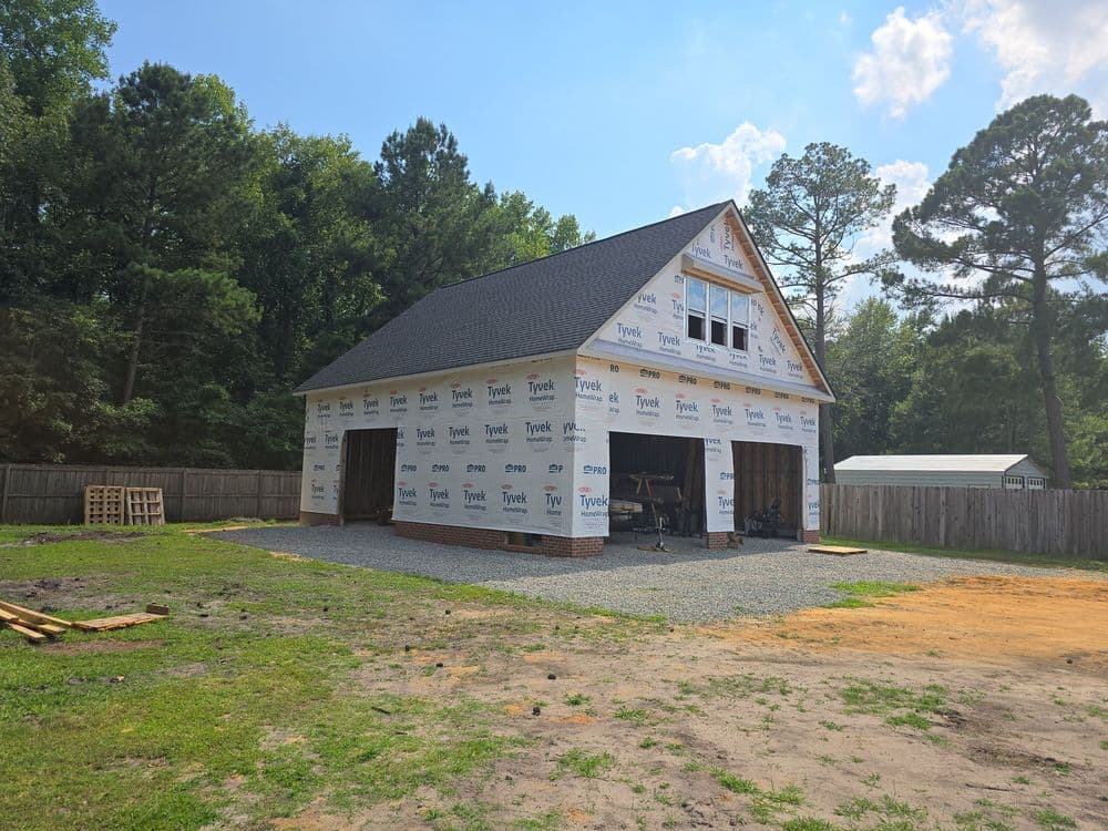 Newly constructed house wrapped in Tyvek house wrap, with gravel driveway and trees in background.