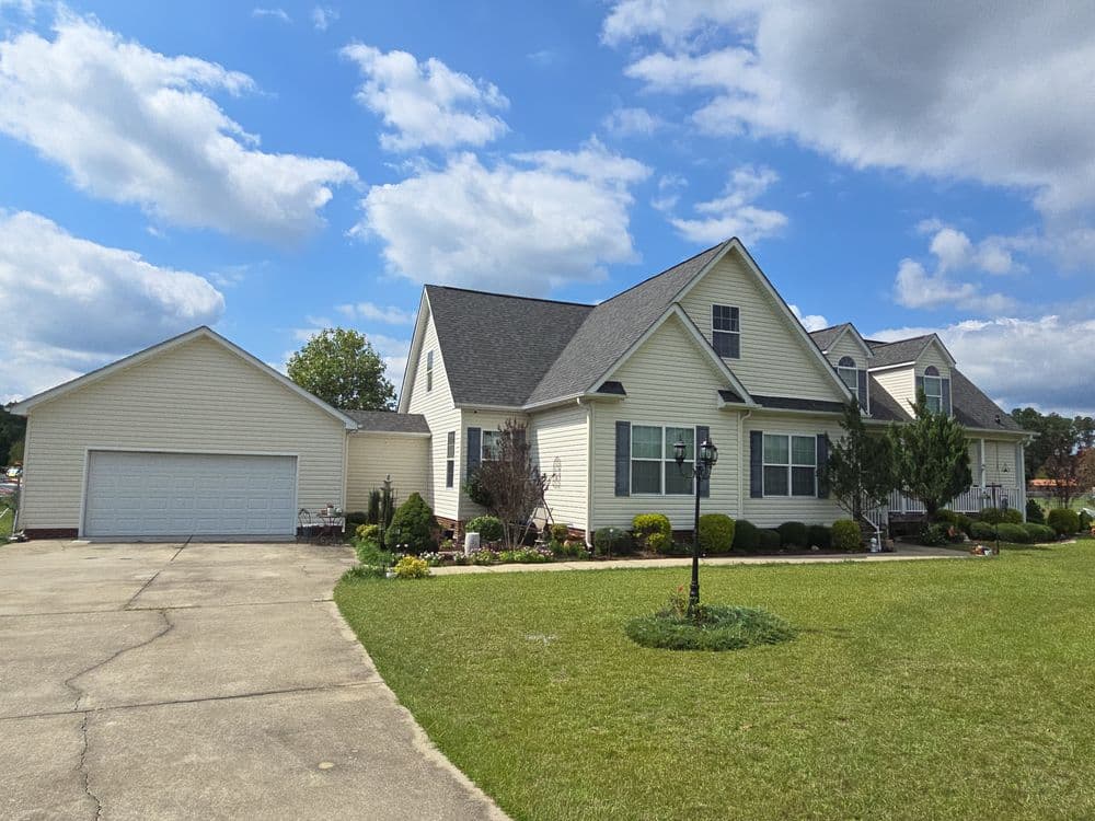 Charming beige house with landscaped yard, two-car garage, and blue sky backdrop.