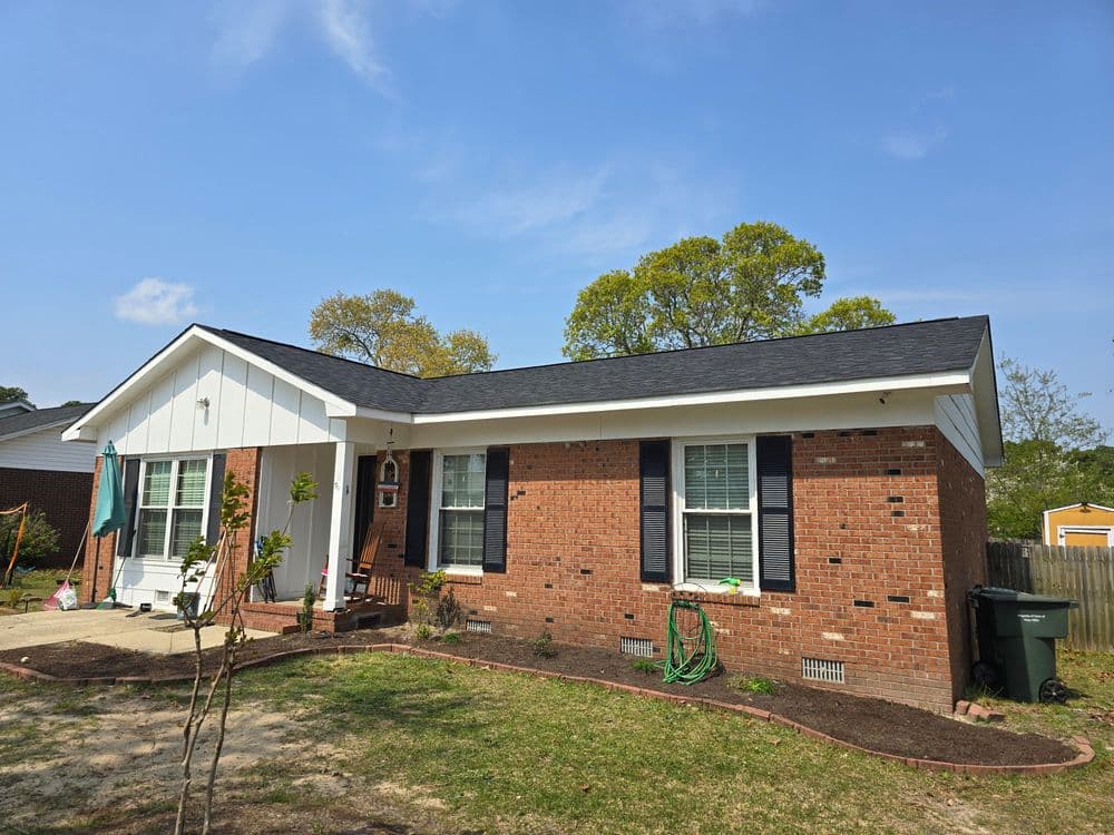 Brick house with white trim, green lawn, and patio under a clear blue sky.