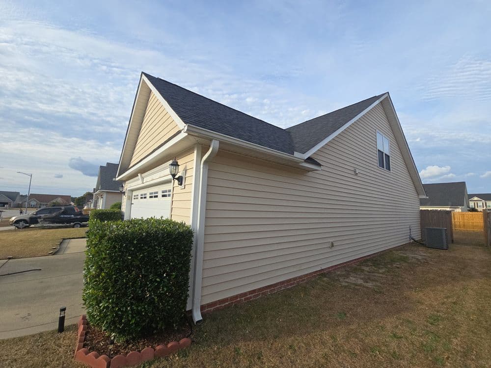 Side view of a beige house with a gray roof and neatly trimmed hedges.
