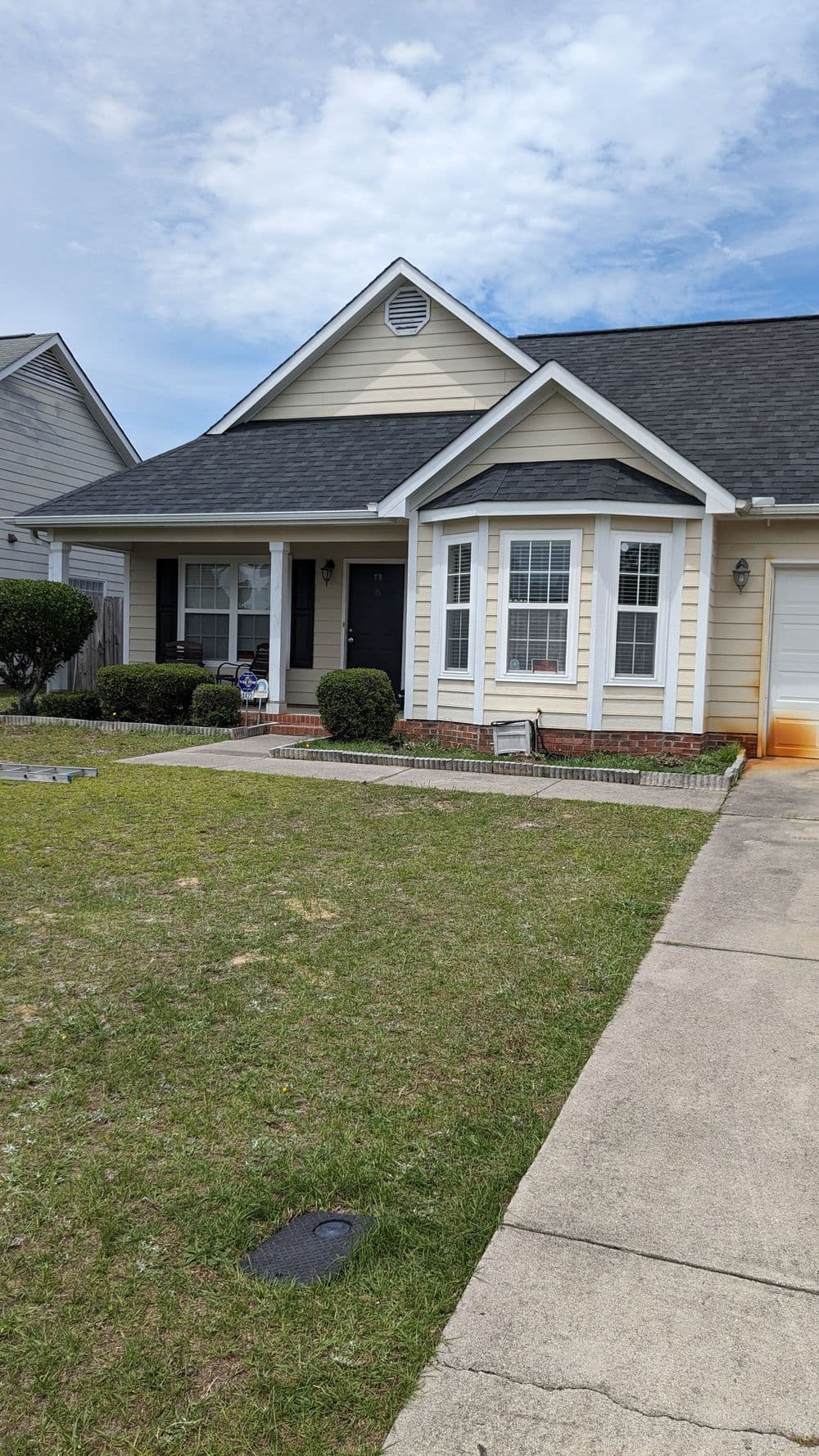 Single-story suburban home with a neat lawn and gray shingles under a cloudy sky.