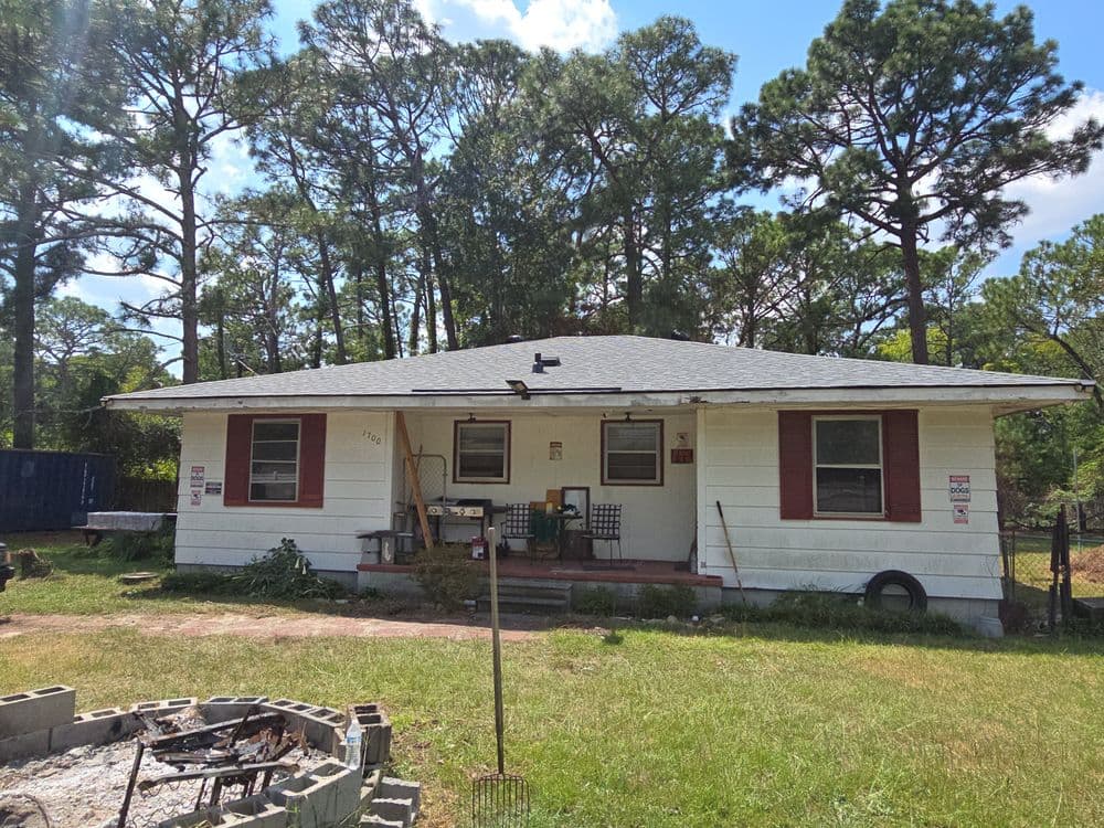Front view of a single-story house surrounded by trees and with a fire pit in the yard.