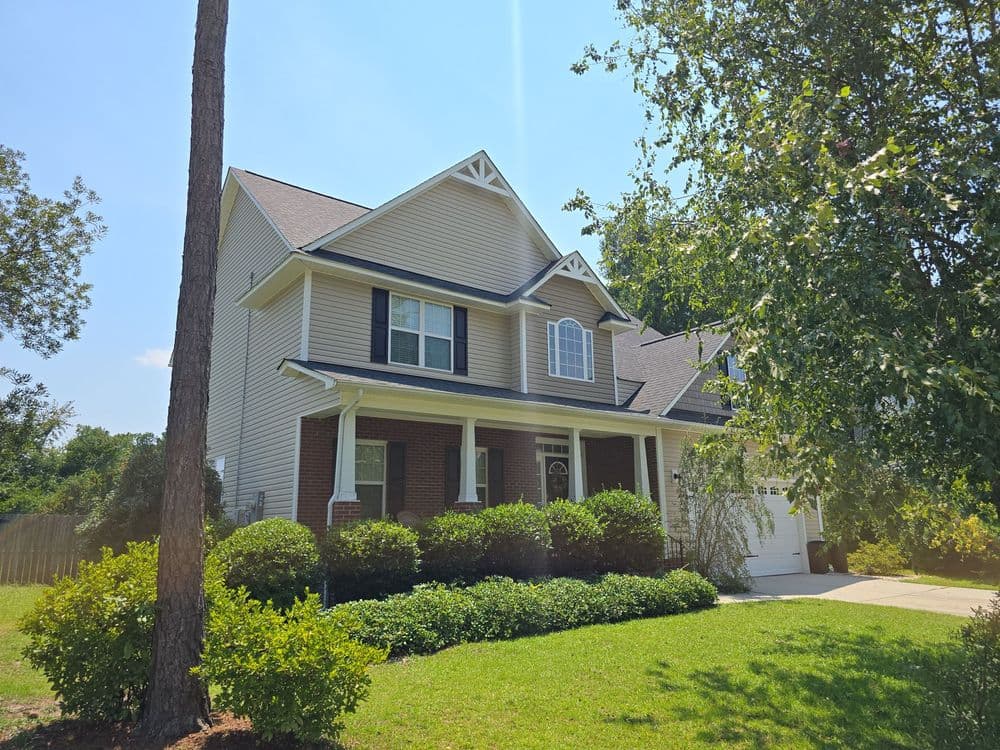 Modern two-story house with a front porch, landscaped yard, and sunny sky.