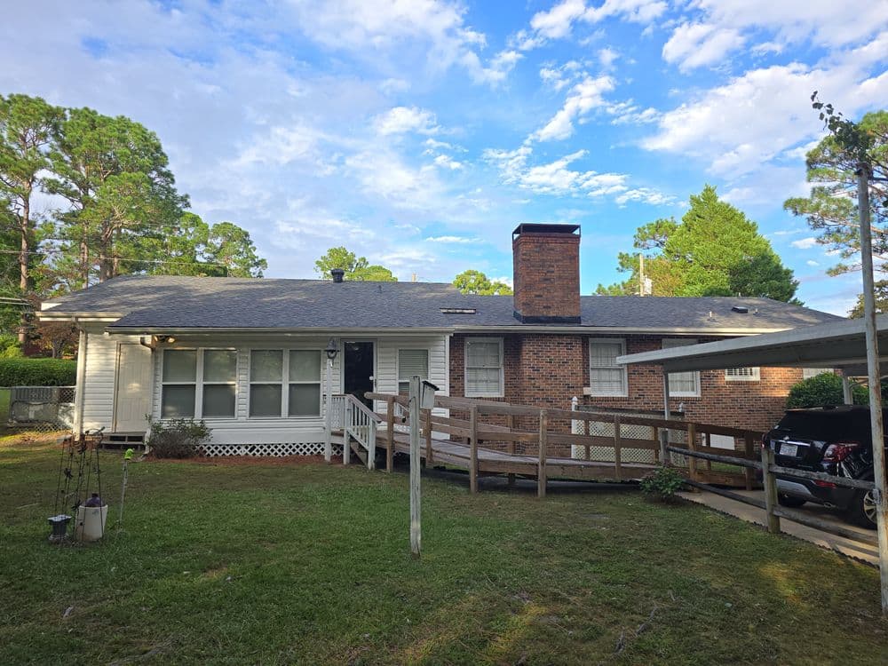 Single-story home with a wooden ramp, brick chimney, and green lawn under a blue sky.