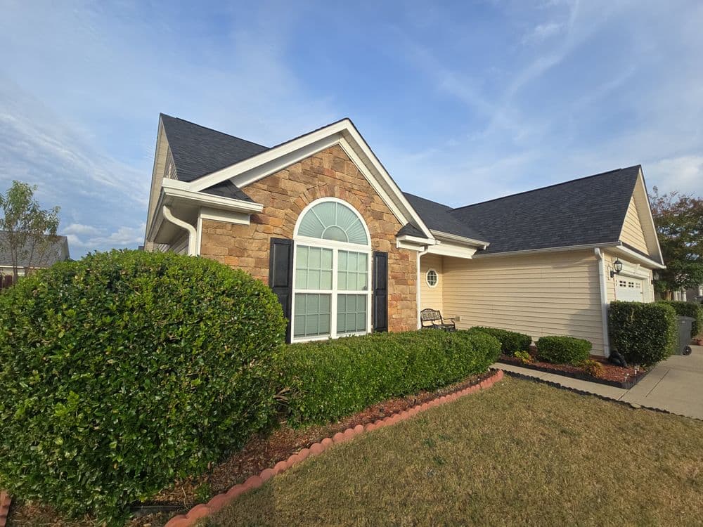 Charming home exterior with stone accents, lush landscaping, and a clear blue sky.