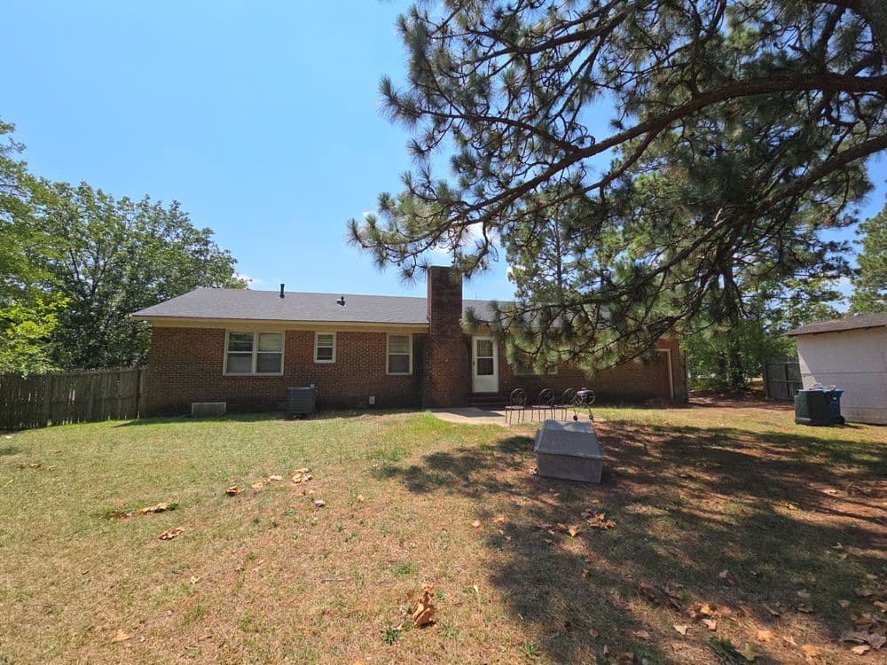 Brick home with backyard trees, sunny sky, and outdoor seating area in a residential setting.