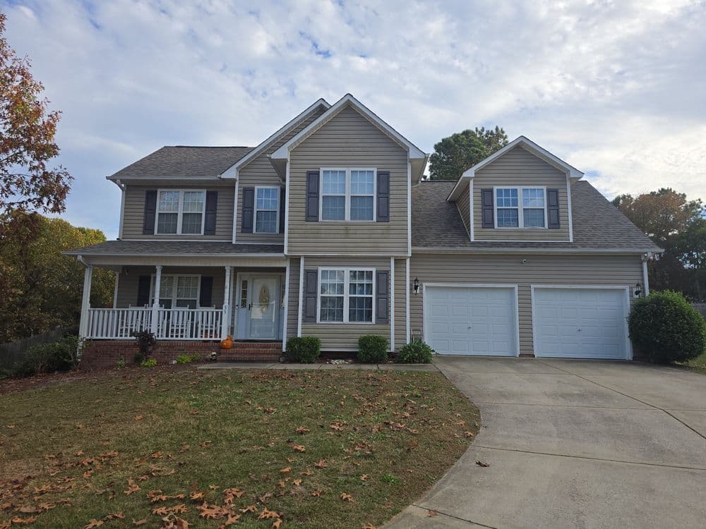 Two-story beige house with a front porch, green lawn, and double garage.