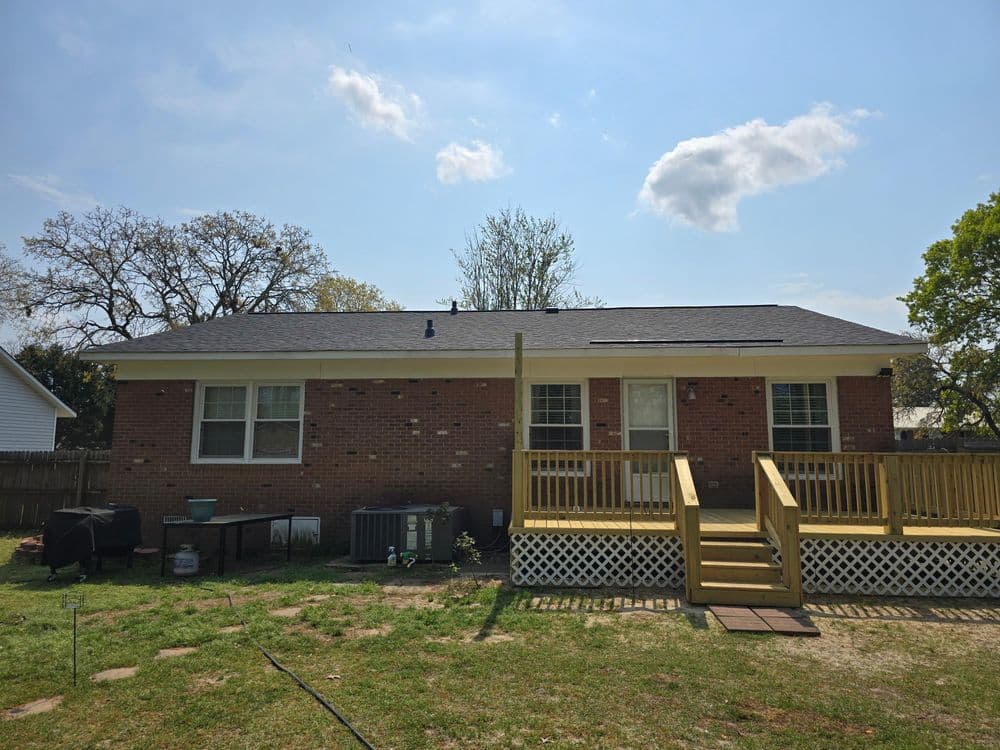 Brick house with a wooden deck, backyard, and clear blue sky on a sunny day.